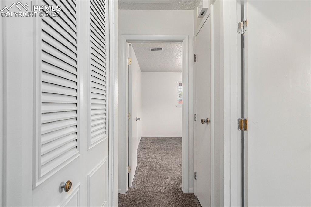 Image 16 of 21: Hallway with visible vents, dark carpet, a textured ceiling, and baseboards