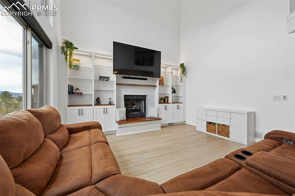 Image 22 of 50: Living area with a high ceiling, a fireplace with raised hearth, and light 
