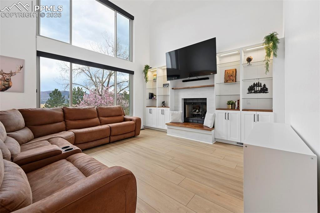 Image 23 of 50: Living room with a high ceiling, light wood-style floors, and a fireplace w