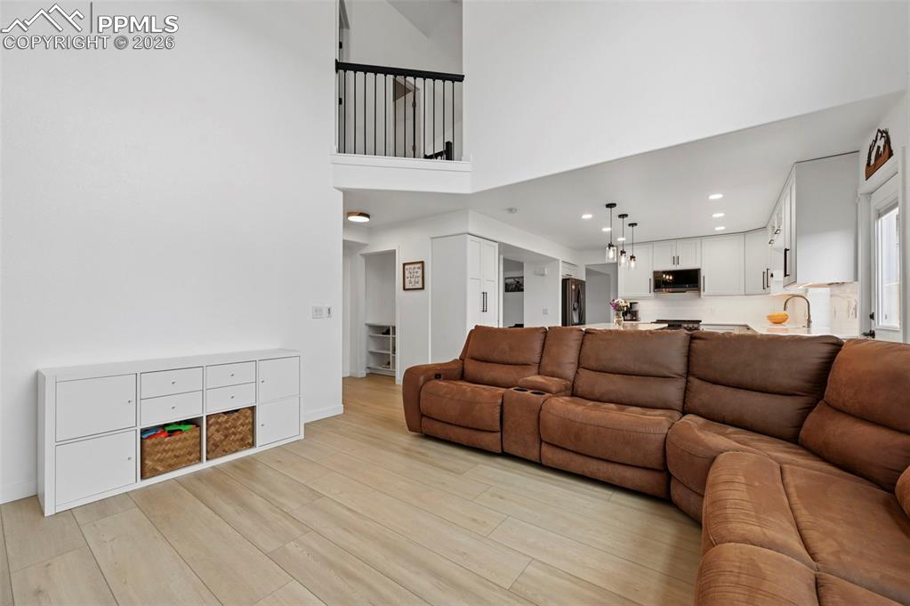 Image 24 of 50: Living room with light wood finished floors, a high ceiling, and recessed l