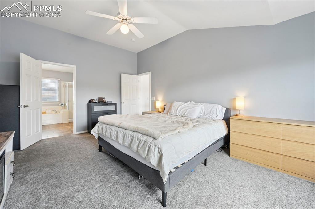 Image 31 of 50: Carpeted bedroom featuring vaulted ceiling, ceiling fan, and ensuite bathro