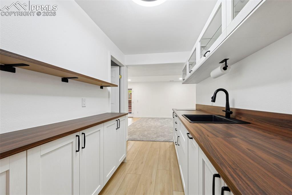 Image 42 of 50: Kitchen with butcher block counters, white cabinetry, open shelves, and lig