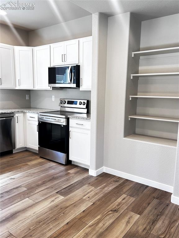 Image 5 of 14: Kitchen featuring stainless steel appliances, white cabinets, dark wood-sty