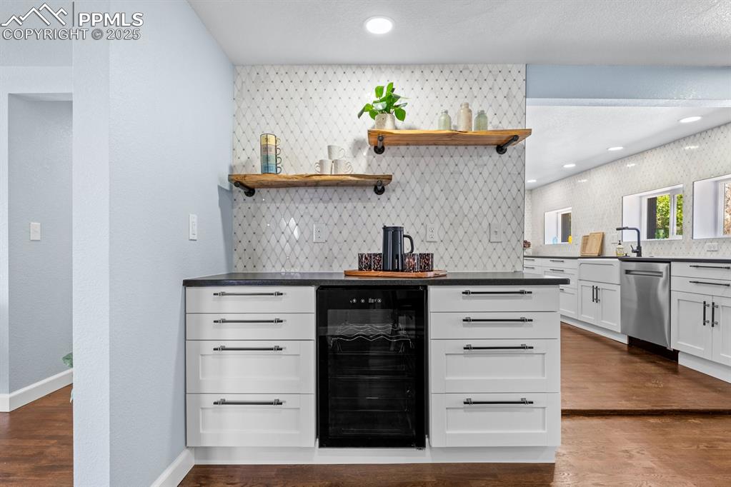 Image 12 of 50: Dining area featuring beverage cooler, decorative backsplash, dark wood-sty