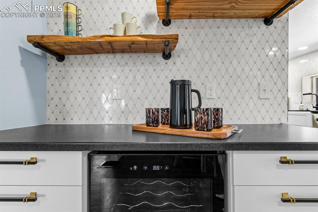 Image 13 of 50: Kitchen with beverage cooler, decorative backsplash, open shelves, white ca