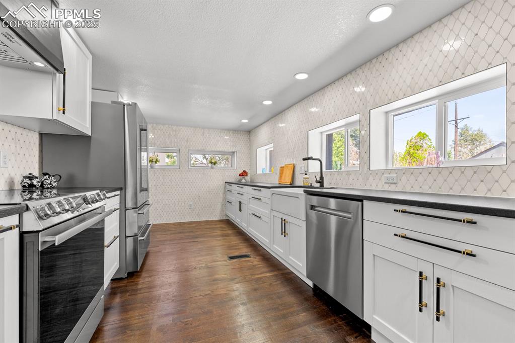 Image 15 of 50: Kitchen with tiled walls, stainless steel appliances, dark granite countert