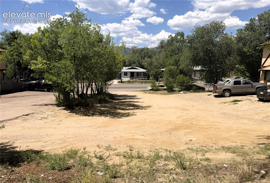 Image 7 of 8: Expansive gravel lot with surrounding mature trees and partial mountain bac
