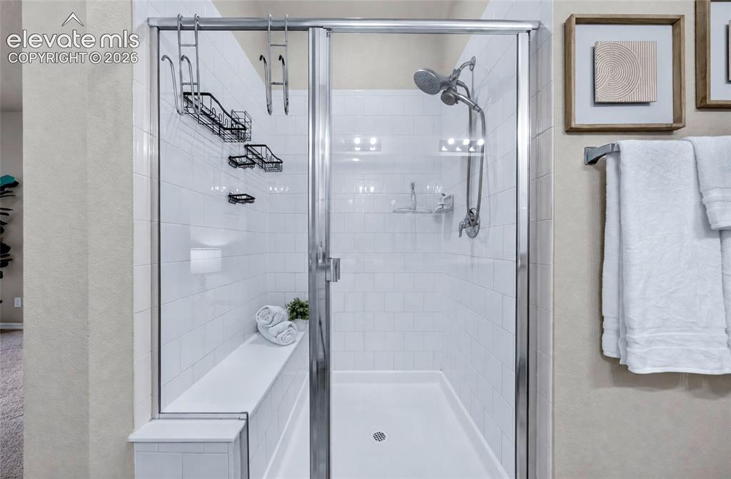 Image 25 of 41: Glass-enclosed shower with subway tile surround, built-in bench, and a mode