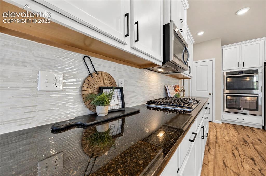 Image 8 of 41: White cabinetry with black hardware, dark stone countertops, stainless stee