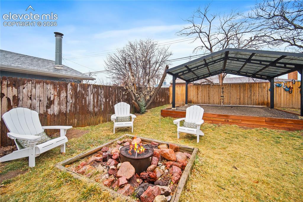 Image 18 of 18: Expansive backyard featuring a fire pit with stone surround, a covered pati