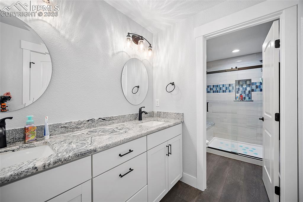 Image 32 of 49: Lower level bathroom with dual vanities, quartz countertops and tile shower