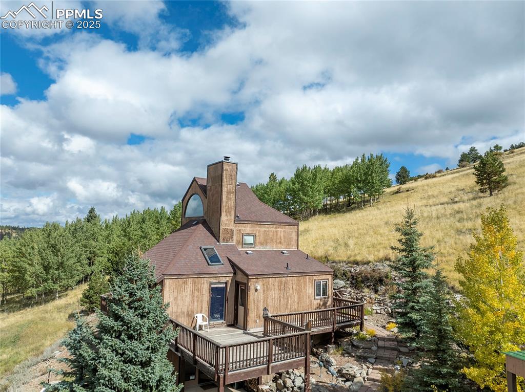 Image 6 of 48: Rear view of house featuring a chimney, a deck, and a shingled roof