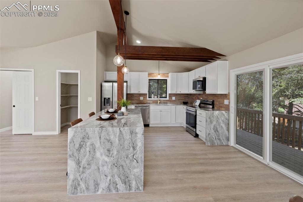 Image 10 of 50: Kitchen with stainless steel appliances, beam ceiling, hanging light fixtur