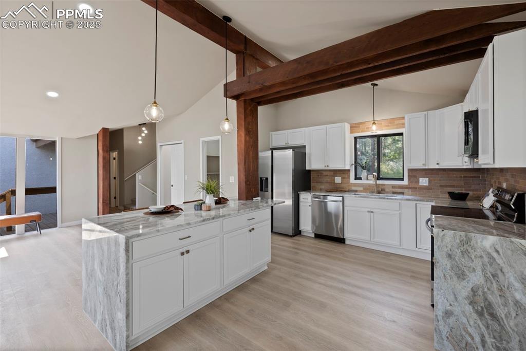 Image 11 of 50: Kitchen featuring decorative light fixtures, white cabinets, light stone co