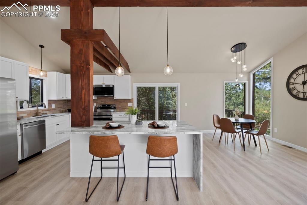 Image 17 of 50: Kitchen with pendant lighting, light stone counters, white cabinetry, backs