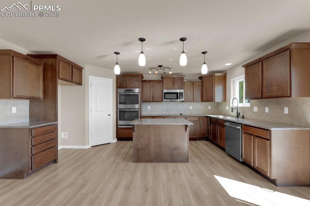 Image 12 of 38: Kitchen with tasteful backsplash, light stone countertops and appliances wi