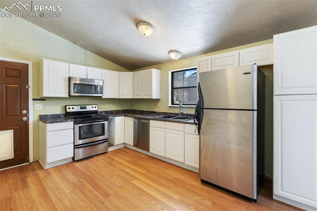 Image 30 of 36: Kitchen with appliances with stainless steel finishes, vaulted ceiling, whi