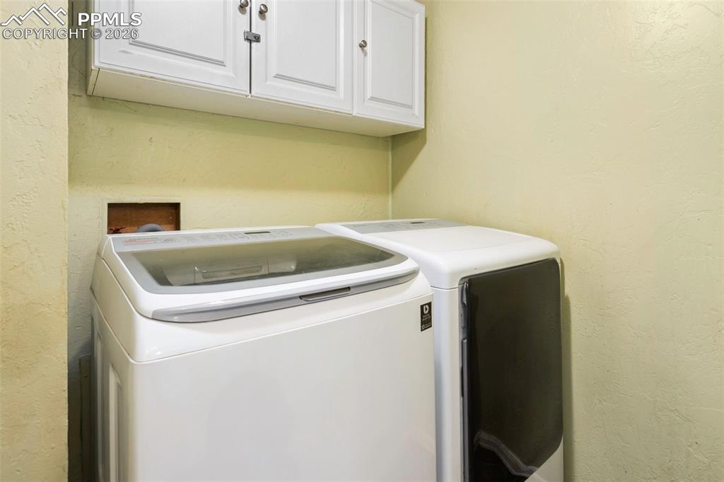 Image 6 of 36: Laundry room with a textured wall, cabinet space, and washer and clothes dr