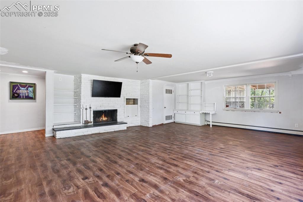 Image 24 of 33: Unfurnished living room with baseboard heating, ceiling fan, a stone firepl