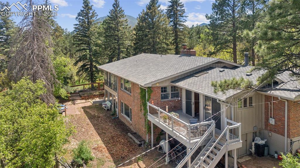 Image 31 of 33: Back of house featuring a shingled roof, brick siding, a chimney, and a woo