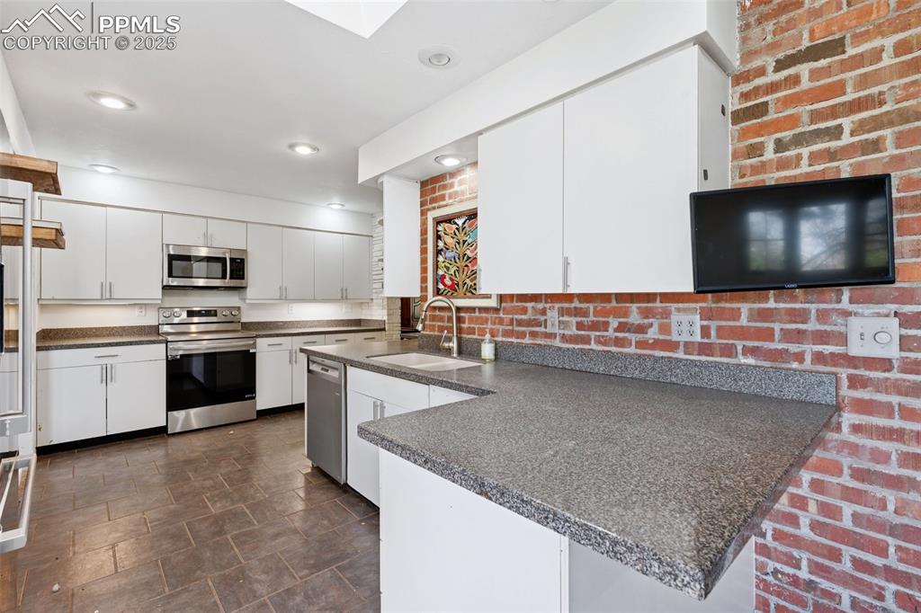 Image 9 of 33: Kitchen with appliances with stainless steel finishes, a sink, dark counter