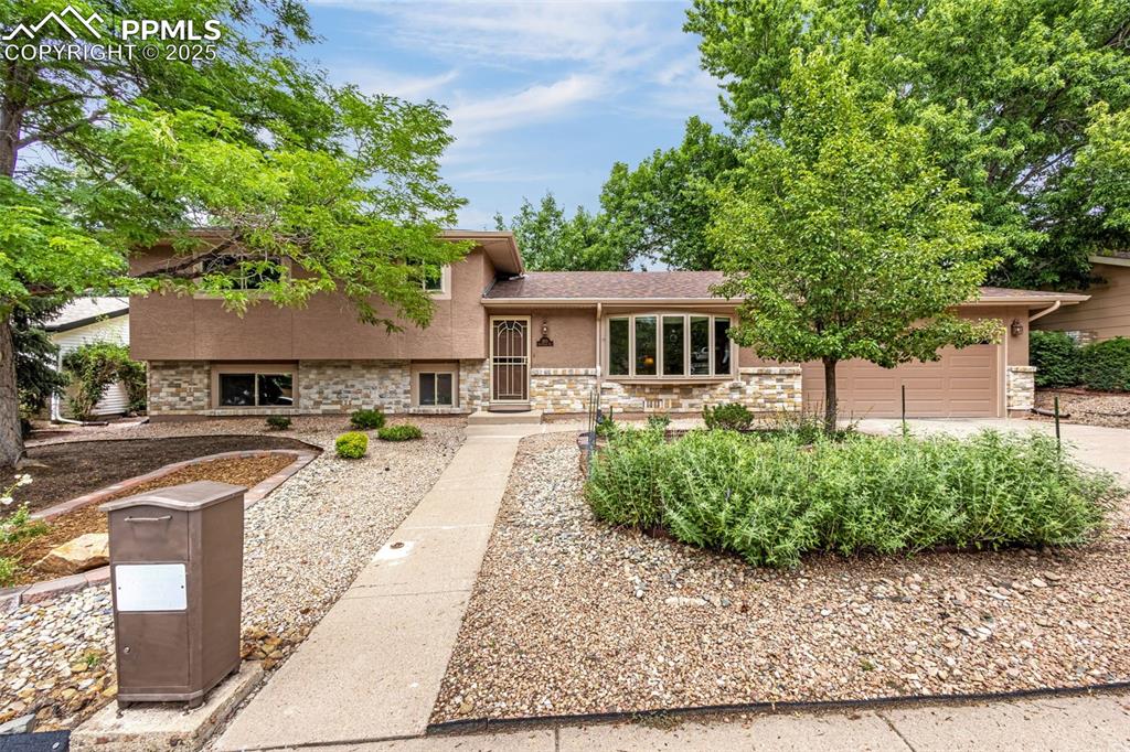 Caption: Split level home with stucco siding, a garage, stone siding, and concrete driveway