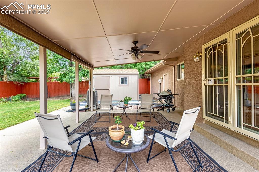 Image 21 of 33: Fenced backyard featuring a patio, a storage shed, and ceiling fan