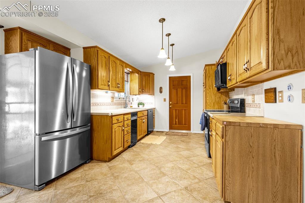 Image 6 of 33: Kitchen with black appliances, light countertops, and brown cabinets
