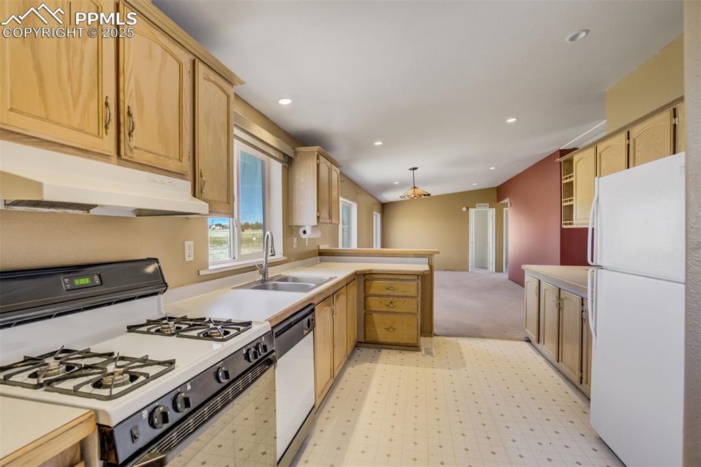 Image 19 of 50: Kitchen featuring a sink, white appliances, a peninsula, under cabinet rang