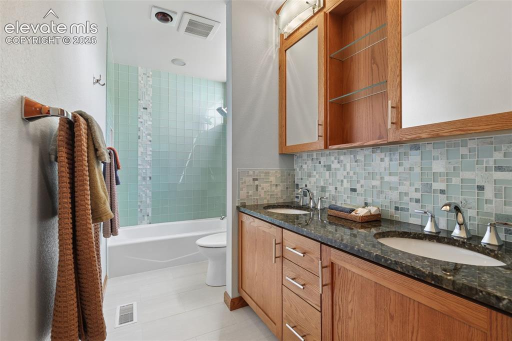 Image 25 of 41: Remodeled bath featuring beautiful glass tile with granite counters, double