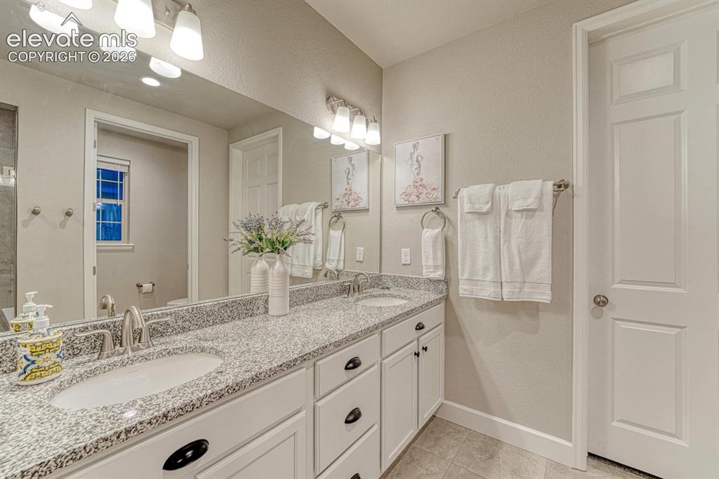 Image 14 of 44: Dual vanity with integrated sinks, granite countertop, white cabinetry, and