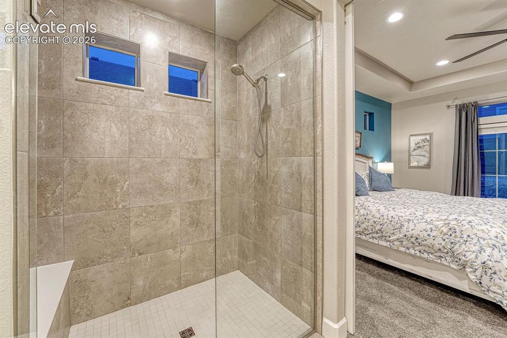 Image 16 of 44: Glass-enclosed shower with tiled walls, integrated bench, and mosaic tile f