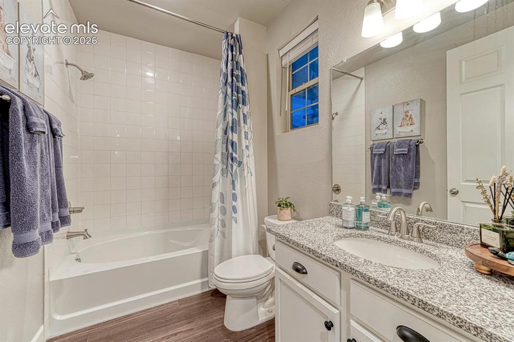 Image 17 of 44: White tile shower surround, integrated bathtub, wood-finish flooring, vanit