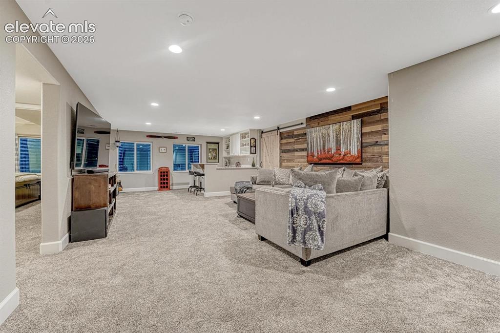 Image 19 of 44: Recessed lighting, wood-finish accent wall, built-in bar with white cabinet