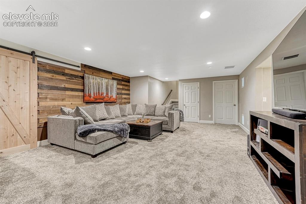 Image 21 of 44: Accent wall with wood paneling, sliding barn door, recessed lighting, carpe