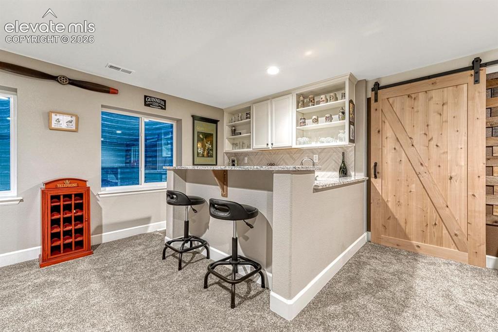 Image 23 of 44: Wet bar with white cabinetry, open shelving, and integrated beverage refrig