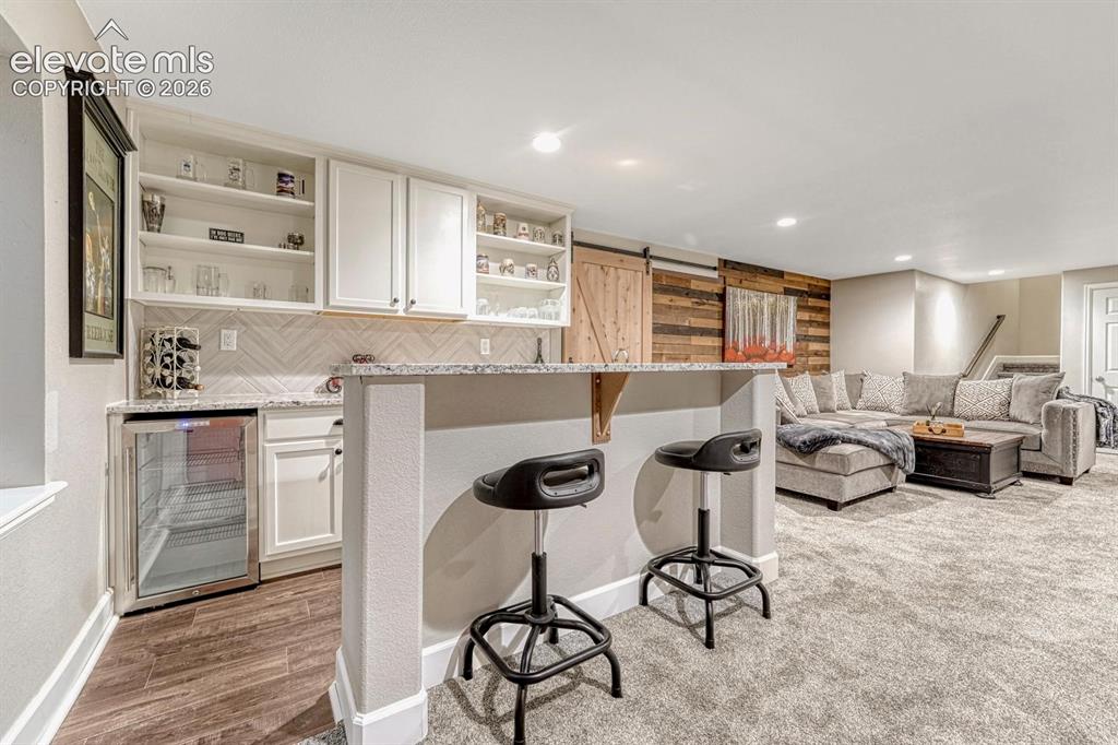 Image 24 of 44: Wet bar with white cabinetry, open shelving, and integrated beverage refrig