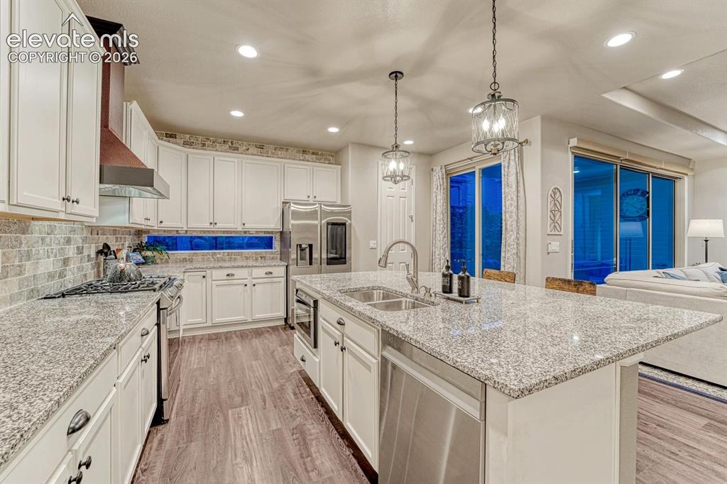 Image 7 of 44: Kitchen featuring white cabinetry, stone backsplash, stainless steel applia