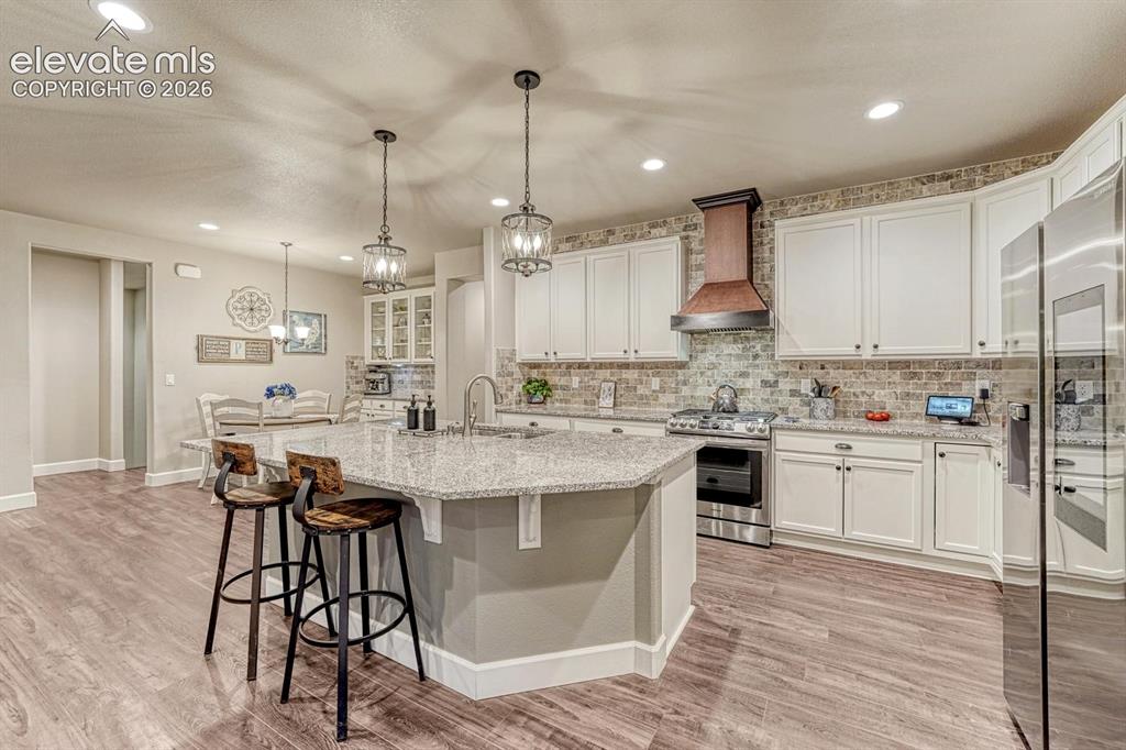 Image 8 of 44: Kitchen featuring white cabinetry, stone backsplash, stainless steel applia