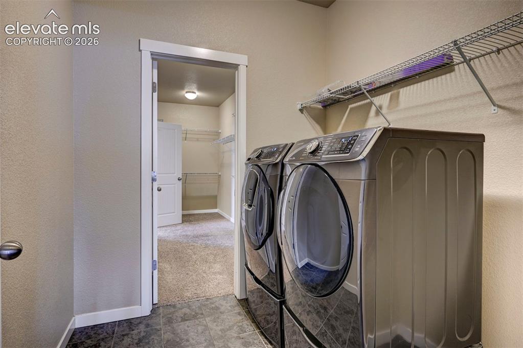 Image 10 of 40: Tiled flooring with laundry appliances, wall-mounted shelving, and a doorwa