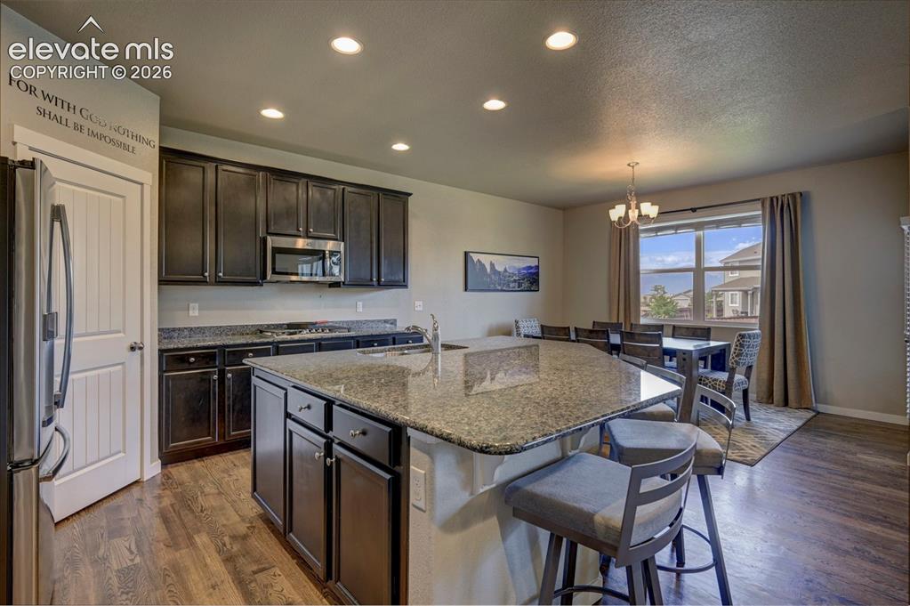 Image 16 of 40: Expansive kitchen island with a stone-finish countertop, dark wood-finish c