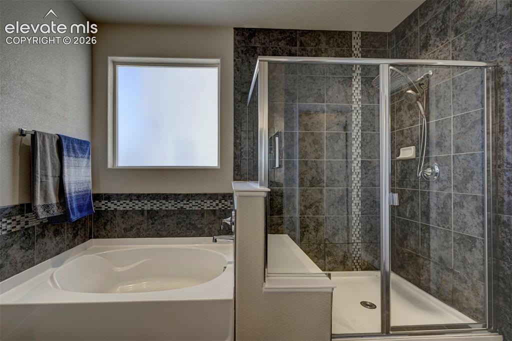 Image 26 of 40: Built-in soaking tub, framed window, glass-enclosed shower, dark tile surro