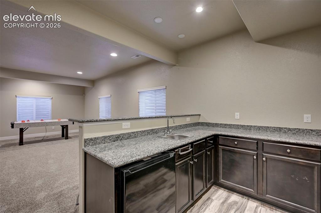 Image 29 of 40: Wet bar with dark cabinetry, stainless steel sink, and stone-finish counter