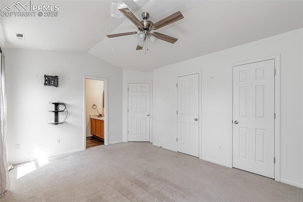 Image 19 of 34: Unfurnished bedroom with lofted ceiling, light carpet, a ceiling fan, ensui