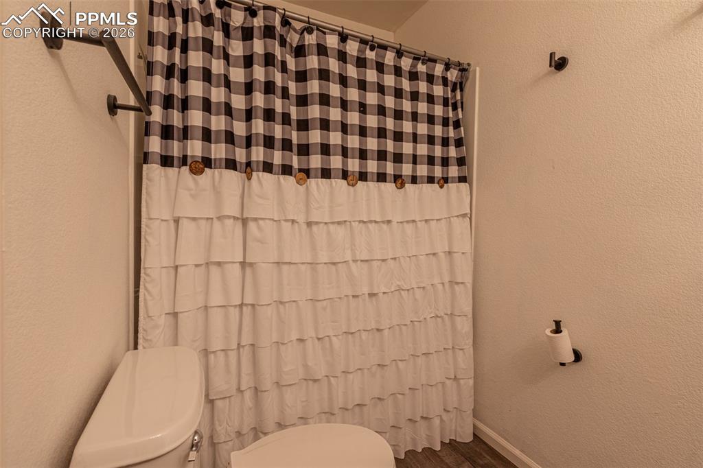 Image 21 of 34: Full bath with a textured wall, a shower with curtain, and dark wood-style 