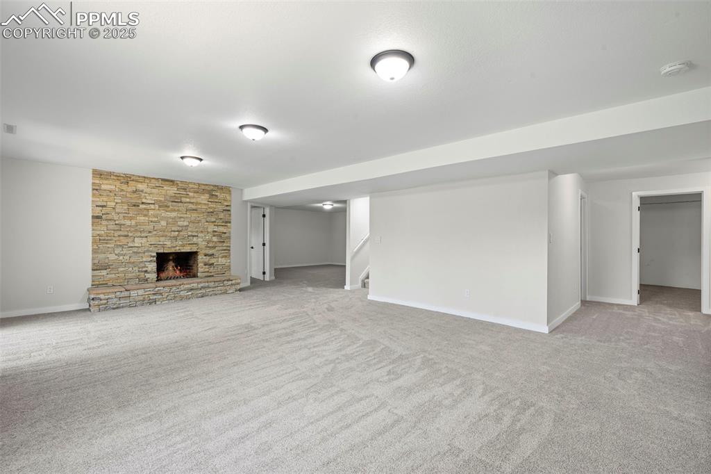 Image 26 of 48: Finished below grade area with light carpet, stairs, and a fireplace