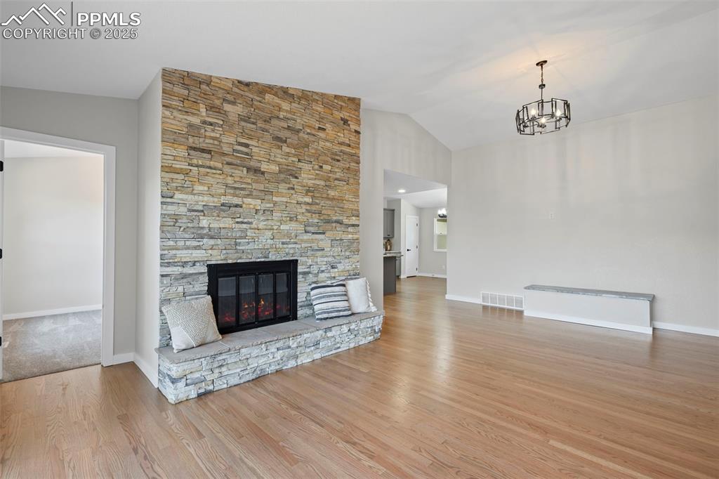 Image 3 of 48: Unfurnished living room with wood finished floors, a chandelier, lofted cei