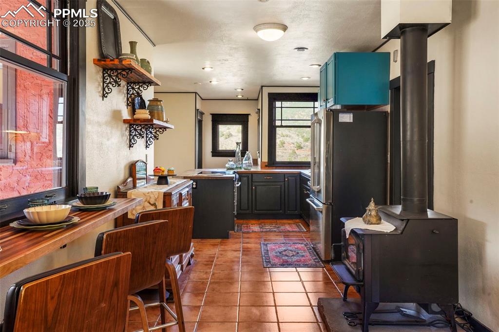 Image 31 of 47: Kitchen featuring a wood stove, open shelves, tile floors, and freestanding