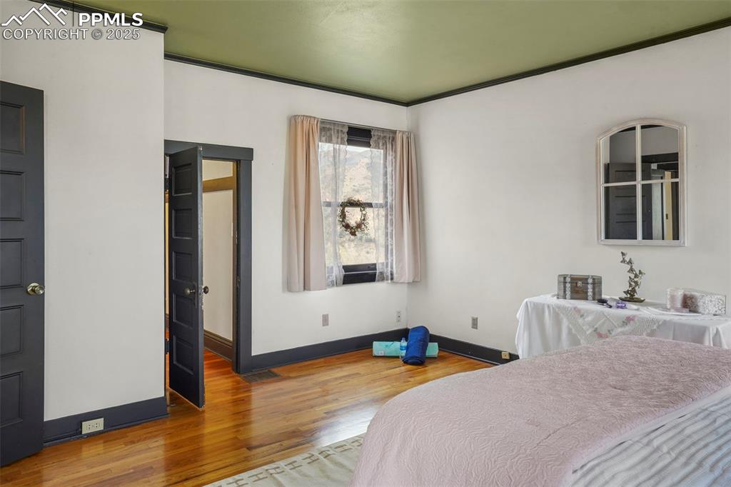 Image 43 of 47: Primary upstairs bedroom with crown molding, wood finished floors, and base