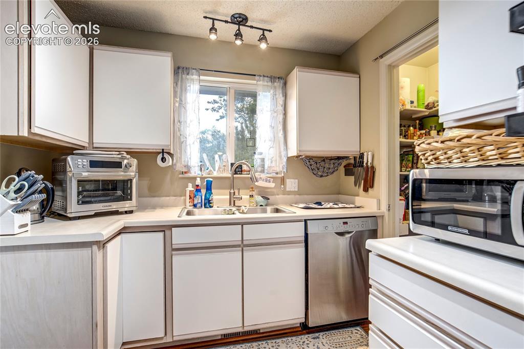 Image 13 of 50: White cabinetry with contrasting trim, stainless steel dishwasher, double b
